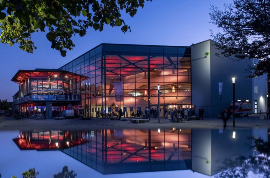 osnabrueckhalle-aussenansicht-event OsnabrückHalle Außenansicht. Event mit Glasfassade und roter Beleuchtung. Spiegelung im Wasser.