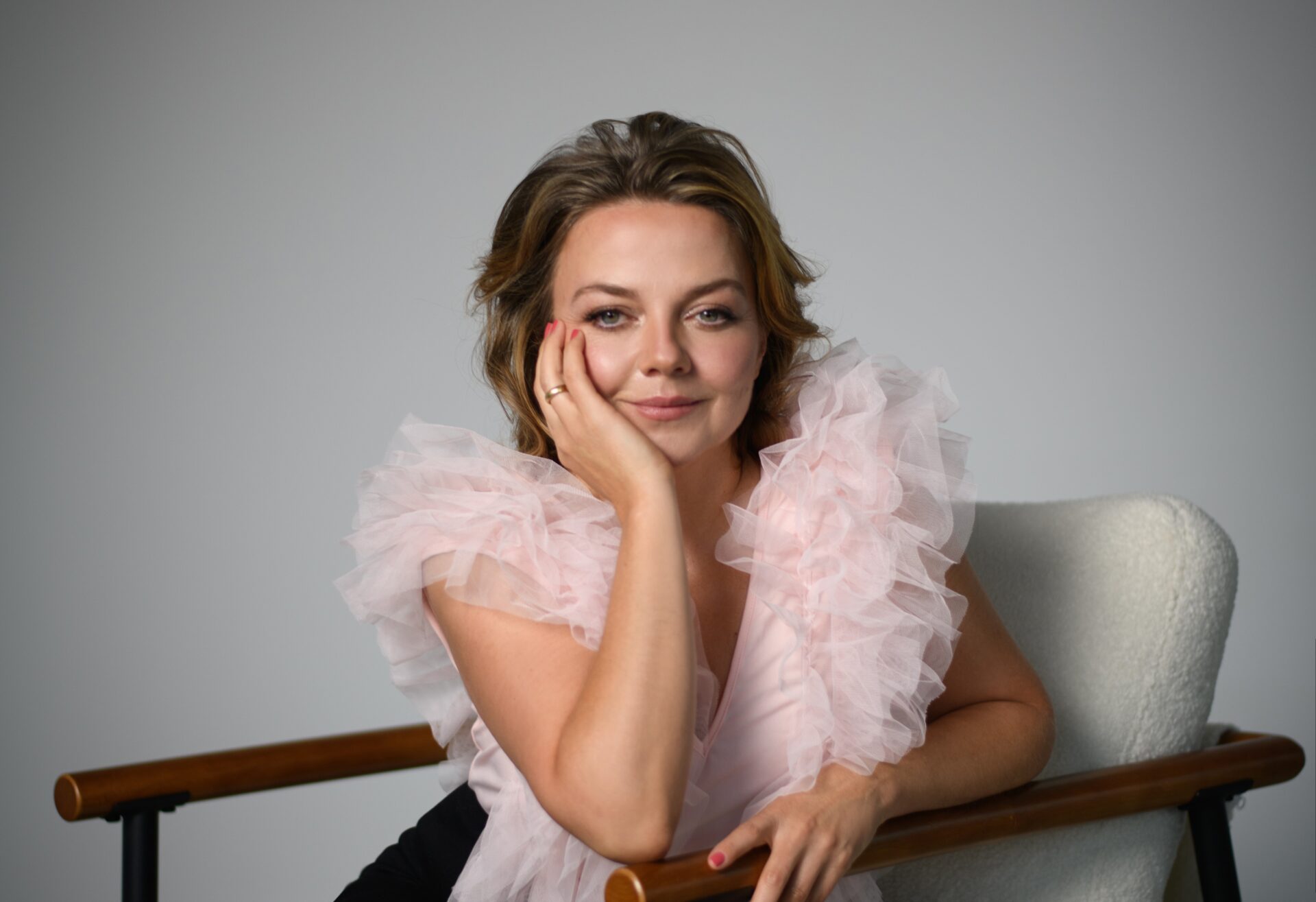 Annett Louisan PR-Foto: Porträt der Sängerin mit rosa Rüschenbluse im Sessel.