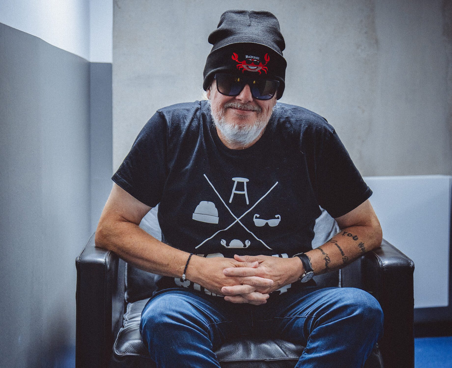 Pressefoto Markus Krebs: Comedian mit Mütze und Sonnenbrille sitzt auf einem Sessel.