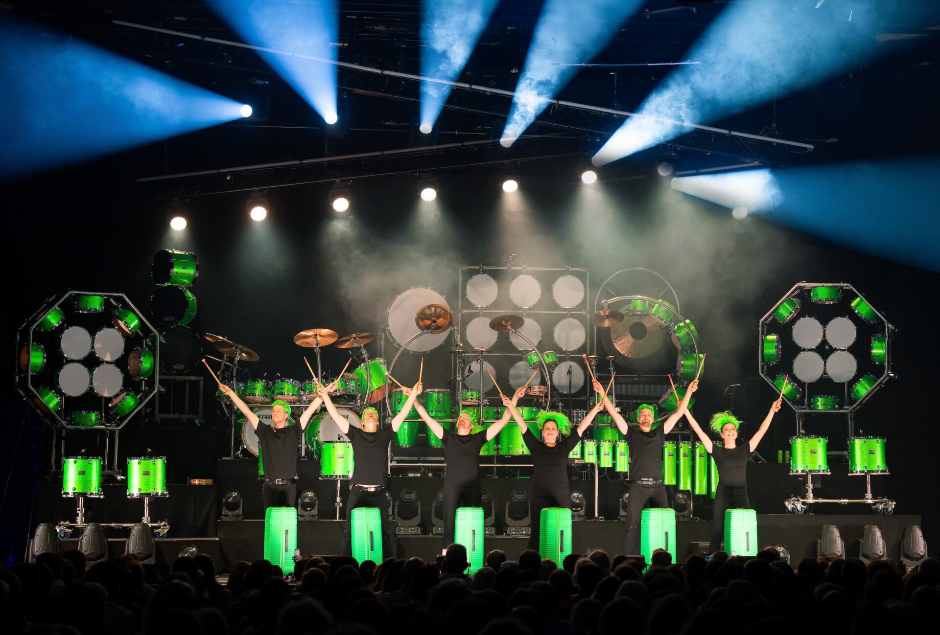 Greenbeats: Schlagzeug-Ensemble mit grünen Instrumenten auf der Bühne, Publikum im Vordergrund.