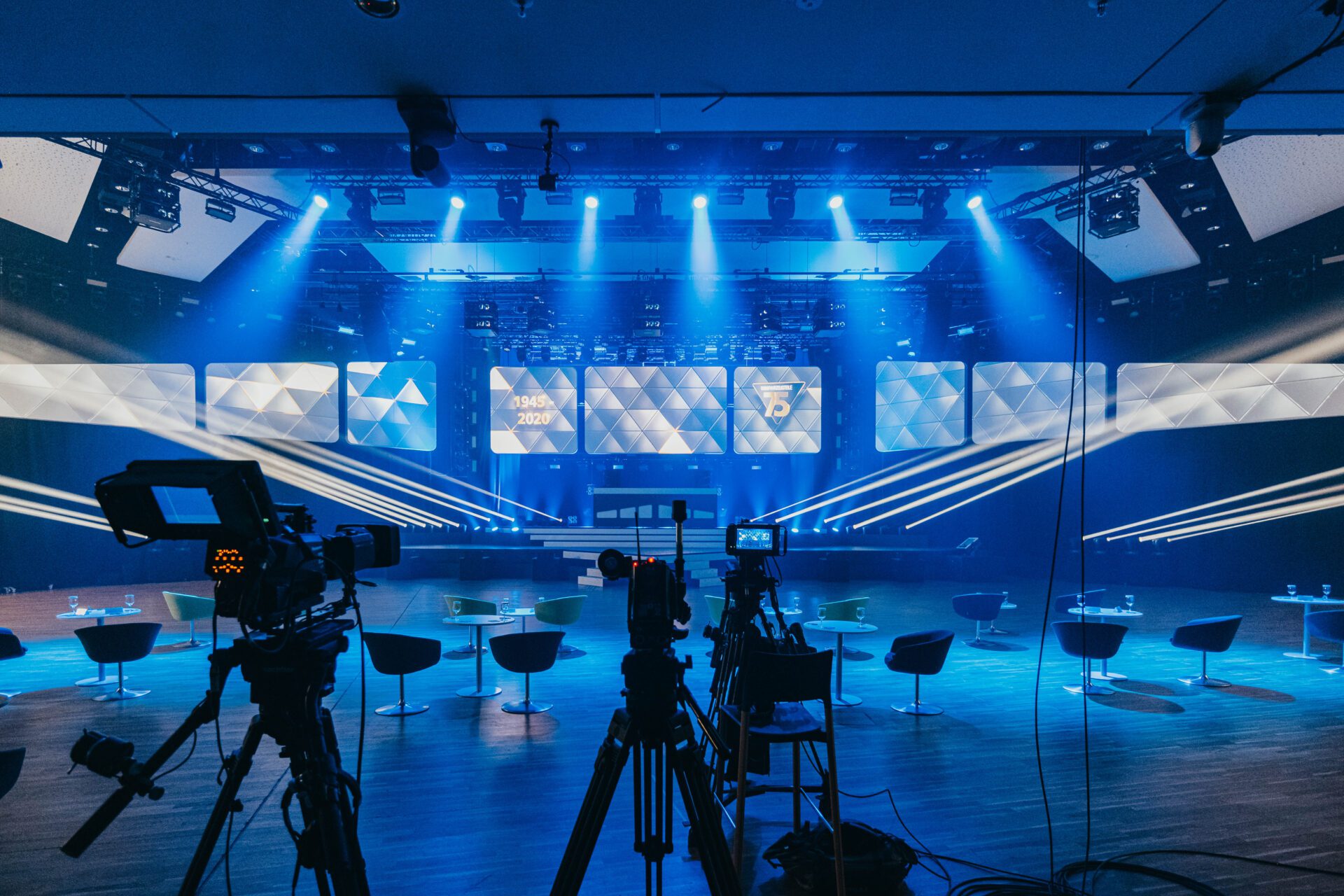 Ansicht VA-Beleuchtung: Eine Bühne mit blauer Beleuchtung und mehreren Kameras im Vordergrund, die auf die Bühne gerichtet sind.