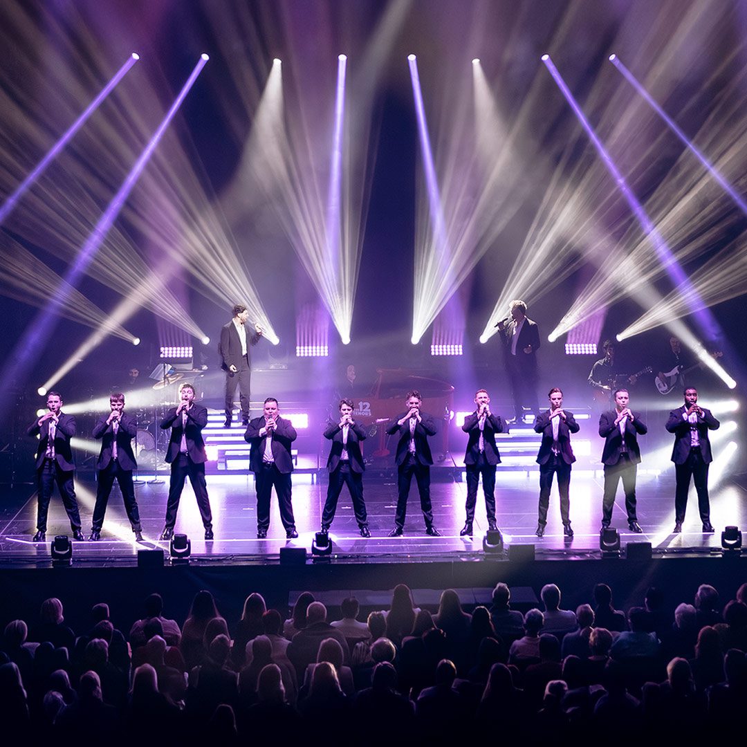 HC_12Tenors_Pressebild01_1080x1080px Die 12 Tenors singen in schwarzen Anzügen auf einer von Scheinwerfern beleuchteten Bühne vor einem Publikum