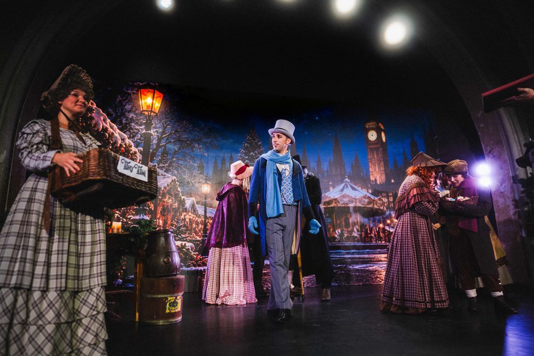 HC_EineWeihnachtsgeschichte_Pressebild01_web Theaterszene der Weihnachtsgeschichte mit Darstellern in viktorianischen Kostümen auf der Bühne vor winterlicher Kulisse